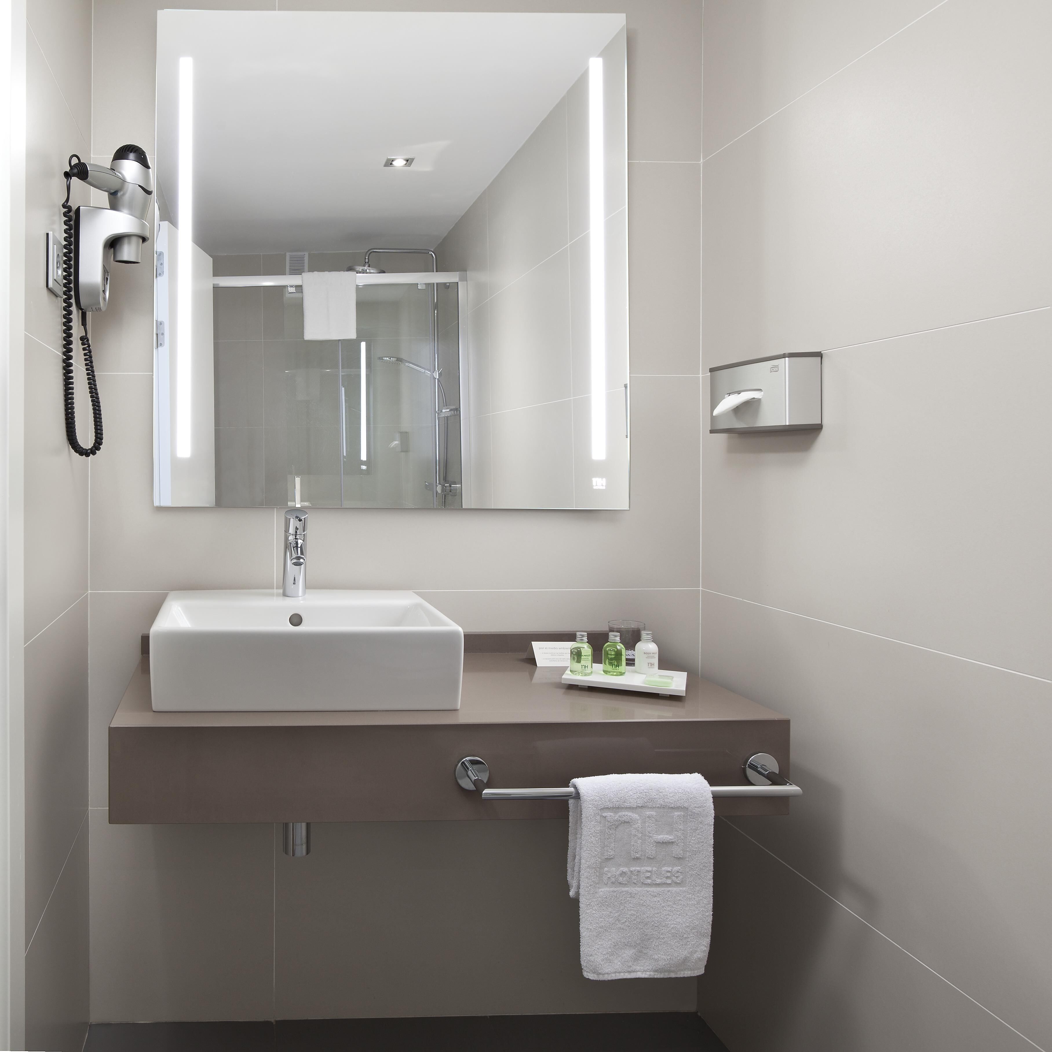Un baño moderno con un espejo grande, un lavabo, un perchero para toallas y un secador de pelo montado en la pared.