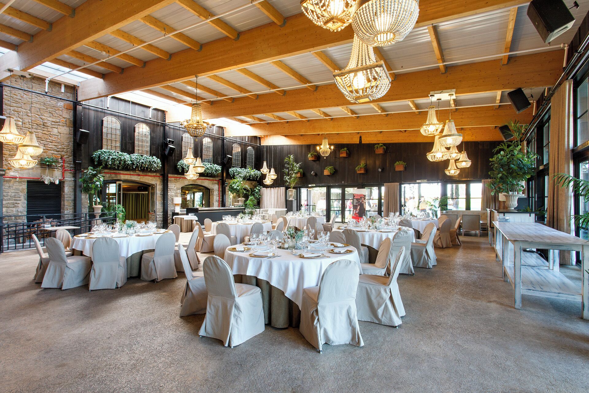 Un espacio interior amplio con techos altos, varias mesas dispuestas para cenar y candelabros de cristal colgantes.