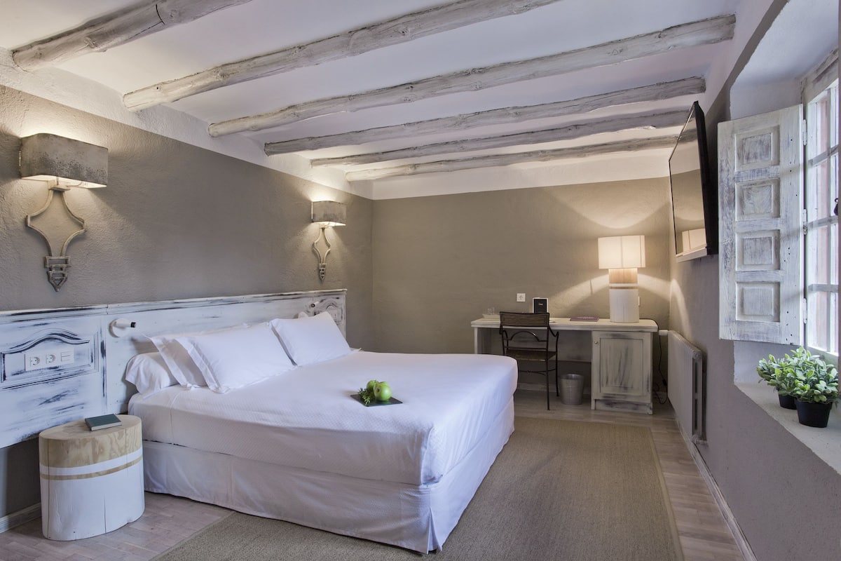 A bedroom with a bed, bedside table, lamp, and a desk with a chair.