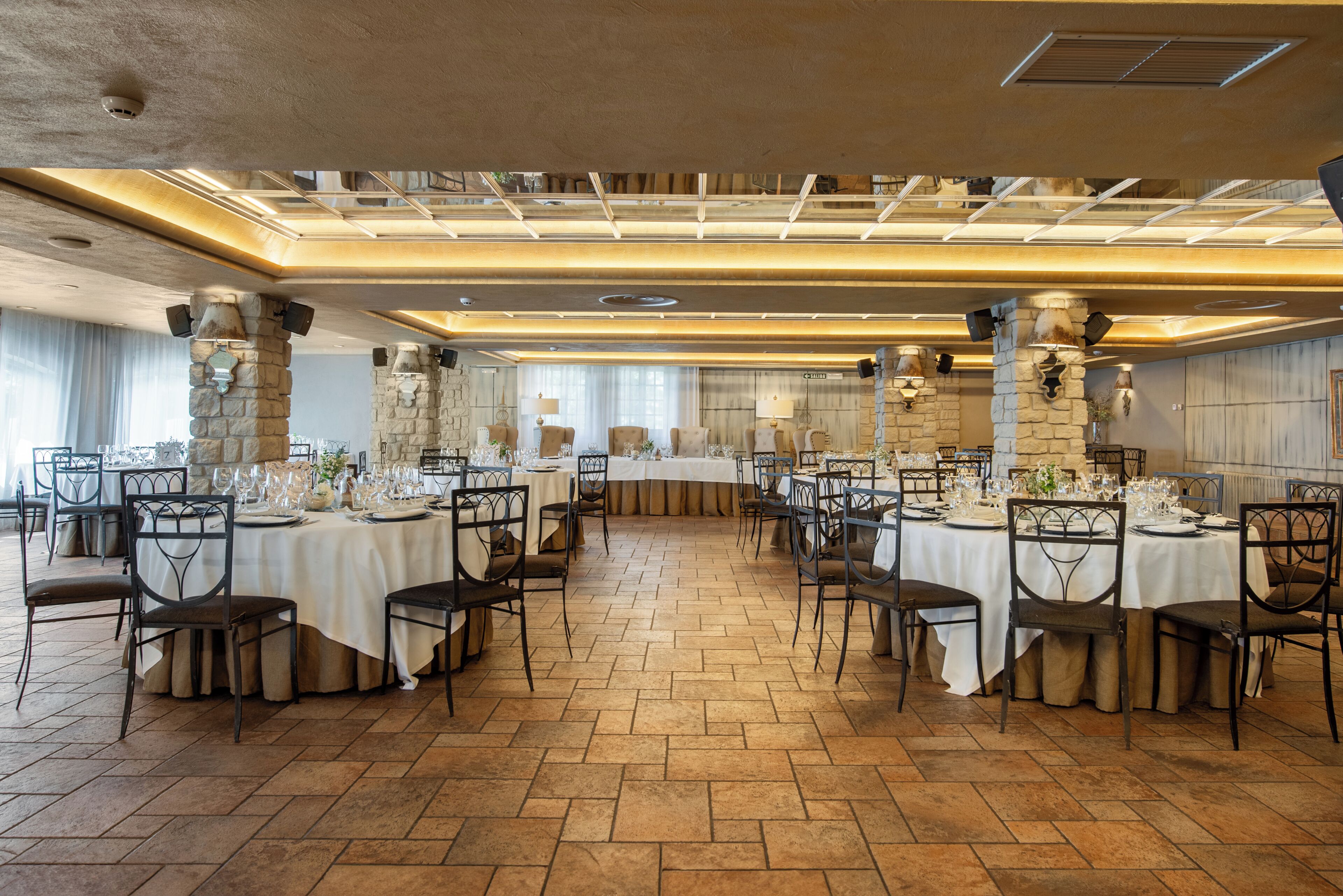 Un salón de banquetes con varias mesas redondas, sillas y un techo alto con tragaluces.
