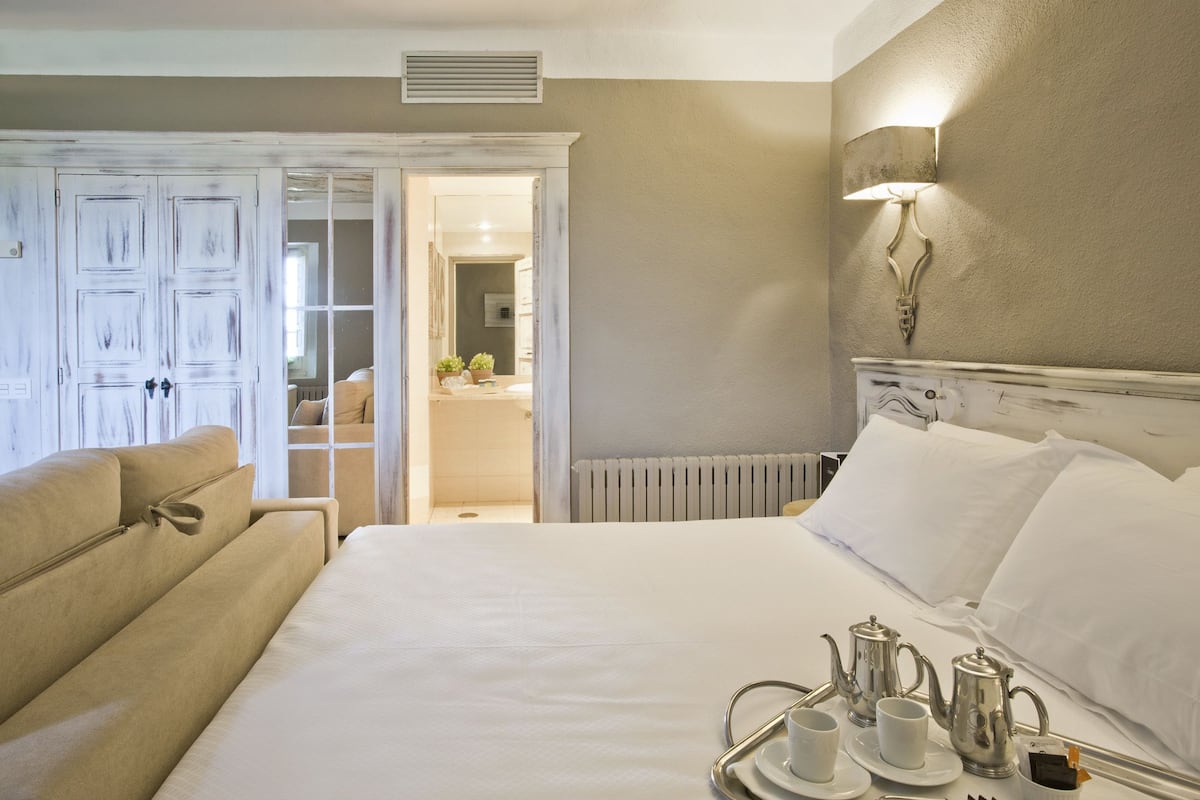 A hotel room with a large bed, a sitting area with a sofa, and a tray with tea and cups.