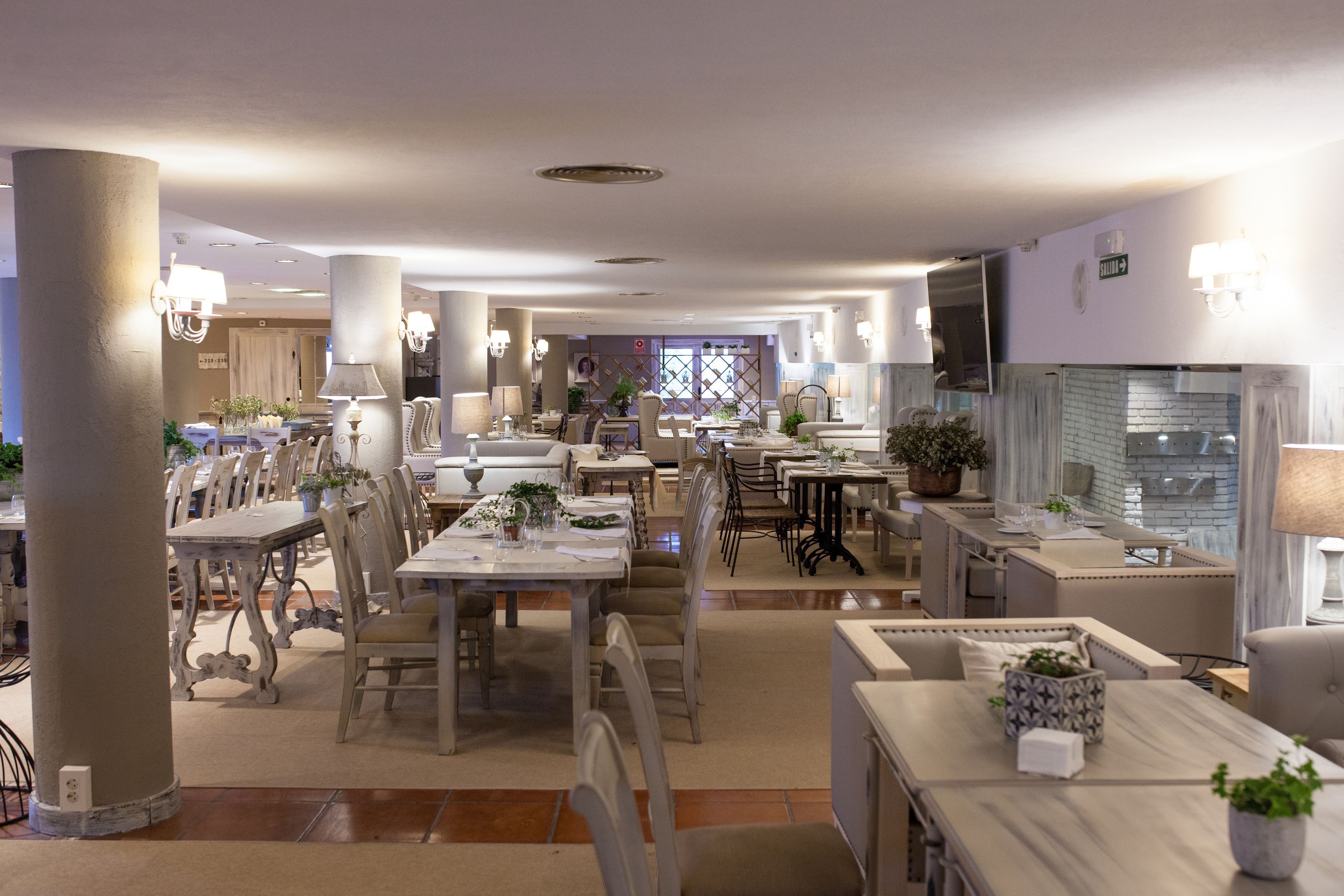 A spacious dining area with multiple tables and chairs, a kitchen area, and a view of the dining room in the background.