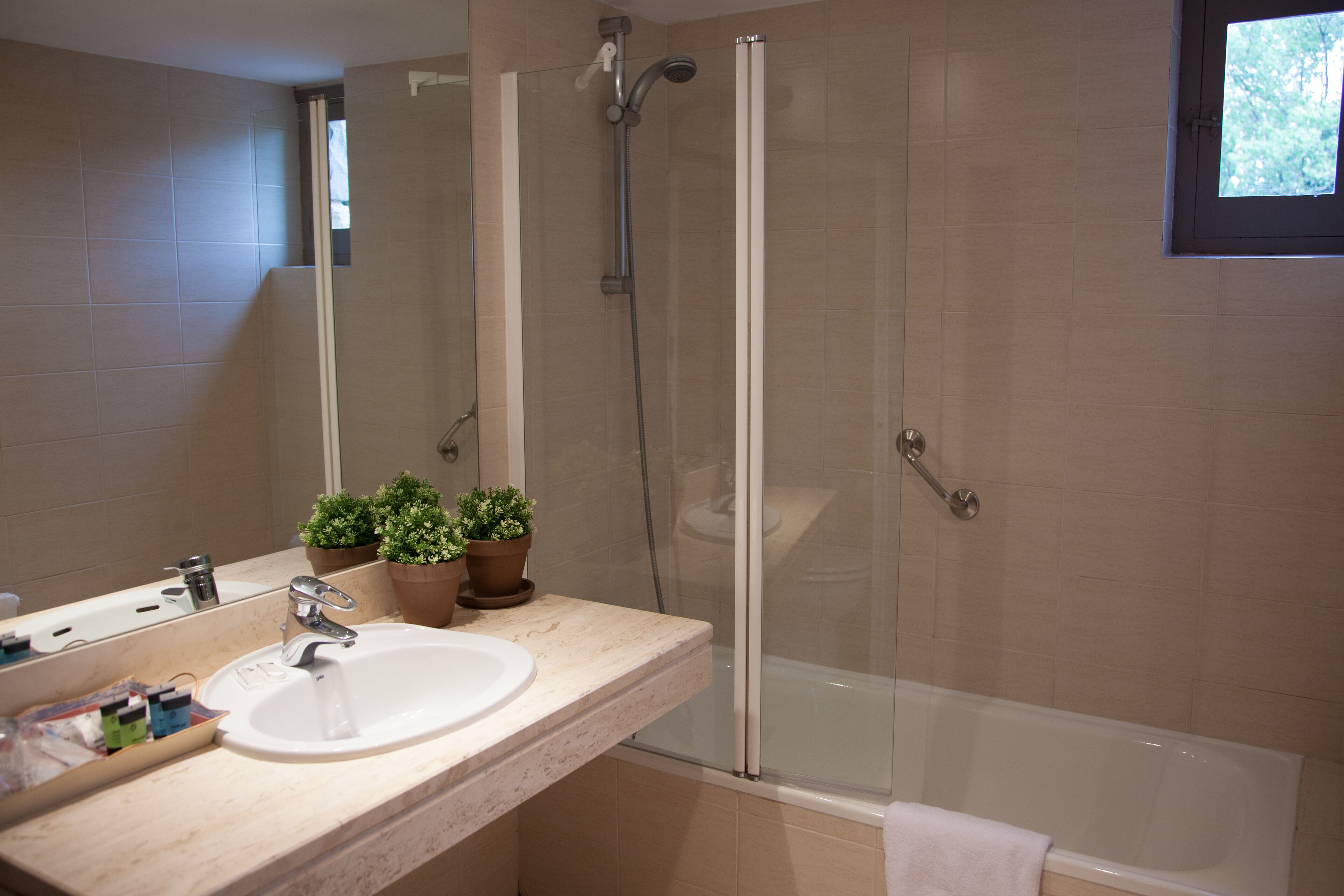 Un baño con lavamanos, espejo, plantas en macetas y cabina de ducha con paredes de vidrio.