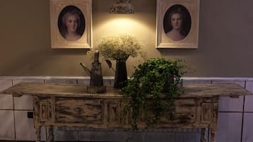 A rustic wooden table with a vase of flowers and a potted plant, set against a wall with framed portraits.