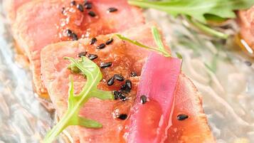 Primer plano de un plato de comida con lonchas de salmón, semillas de sésamo negro y verduras encurtidas rosadas.