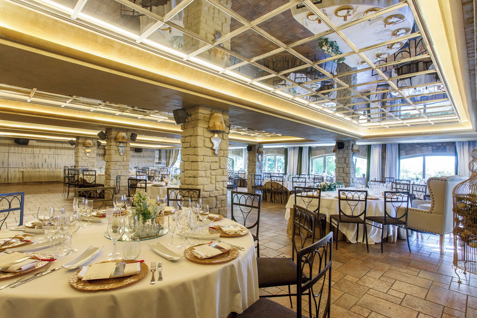Un restaurante con mesas redondas, pilares de piedra y un techo alto con un panel de vidrio.