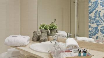 A bathroom with a sink, mirror, and shower. There are towels and toiletries on the counter.
