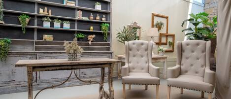 Une pièce avec une table en bois rustique, deux fauteuils rembourrés, une bibliothèque avec des plantes et un miroir.