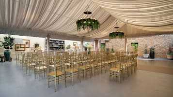 A tented event space with rows of gold chairs, hanging greenery, and a stone wall.