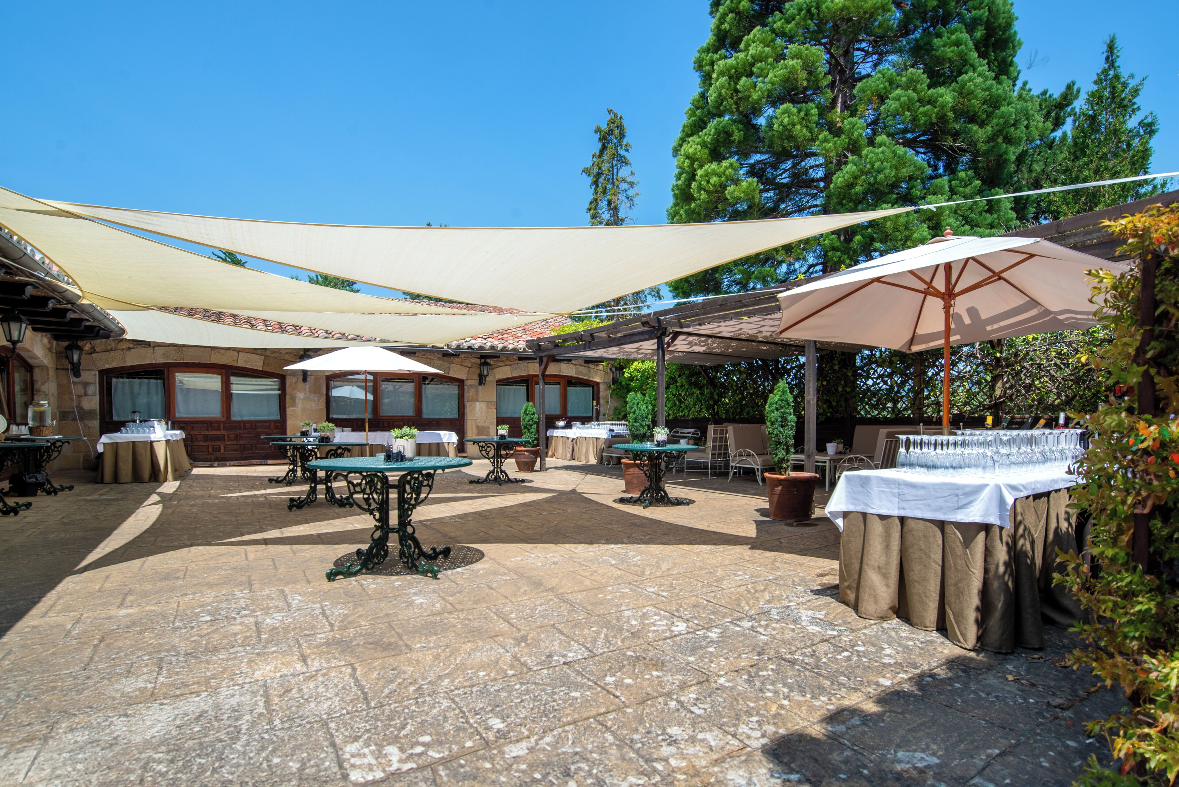 An outdoor patio area with tables and chairs, surrounded by trees and covered by large umbrellas.