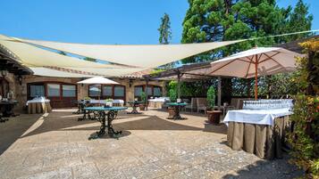 An outdoor patio area with tables and chairs, surrounded by trees and covered by large umbrellas.