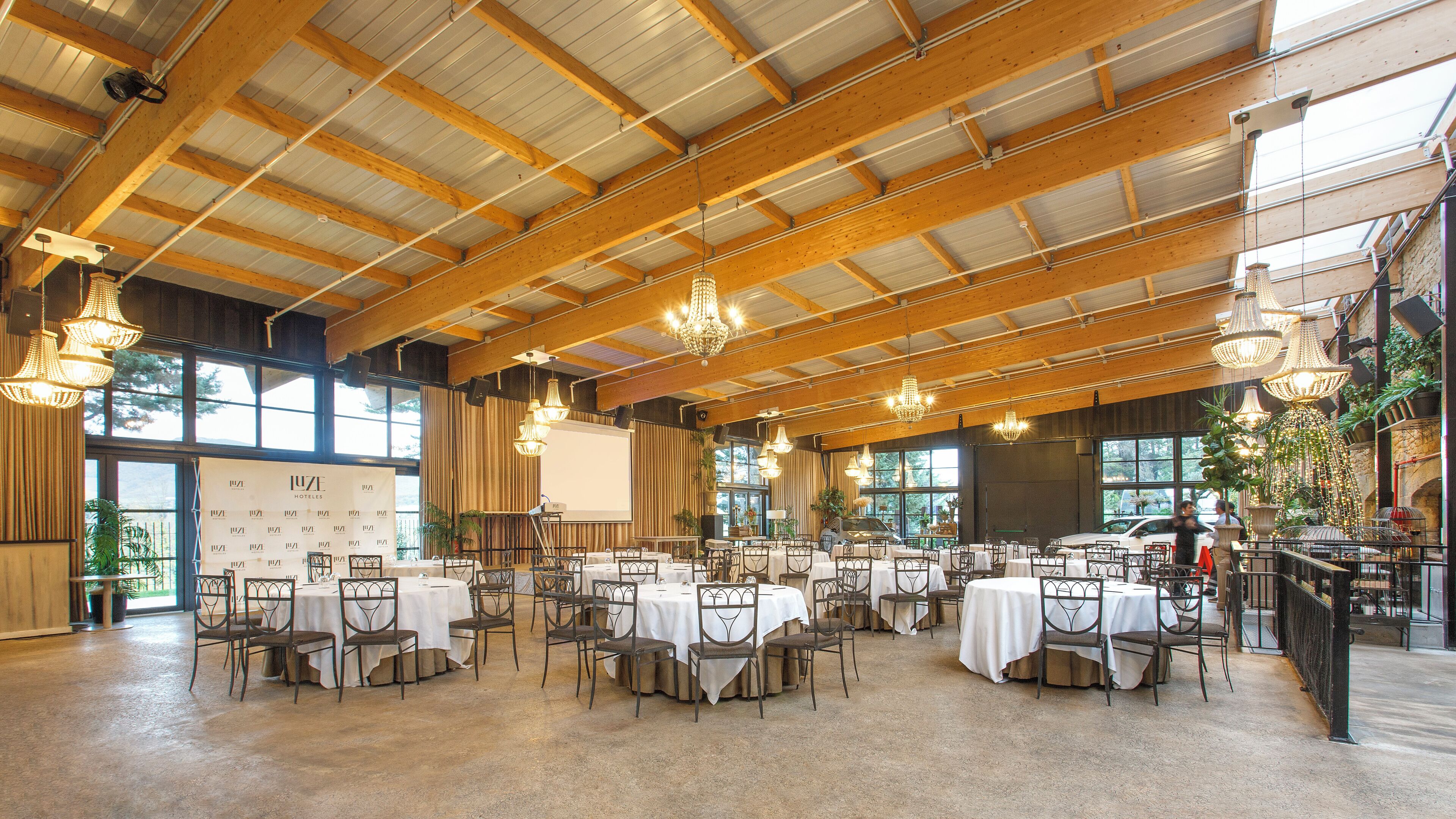 A spacious indoor venue with high ceilings, multiple tables set for dining, and large windows allowing natural light.