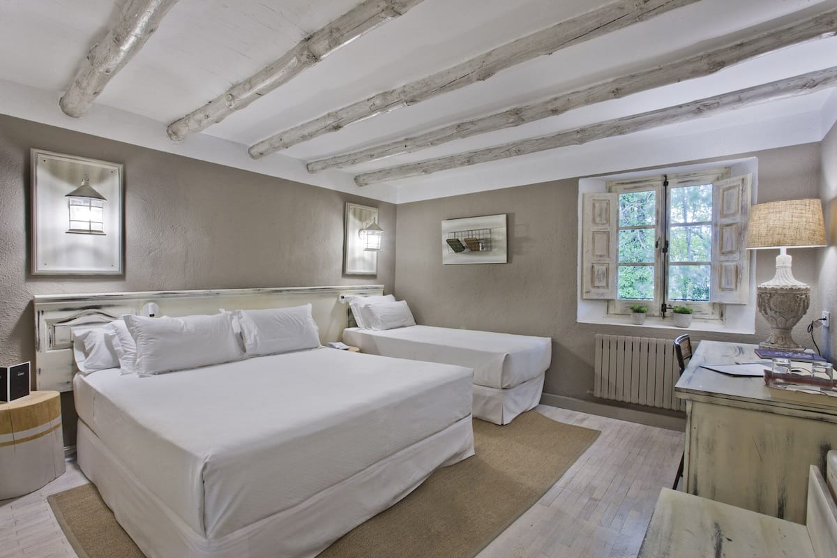 A bedroom with two beds, a radiator, a window with shutters, and a lamp.