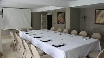 A conference room with a long table, chairs, a projector screen, and a door leading to a salon.