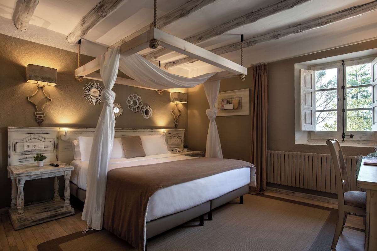 A bedroom with a canopy bed, bedside lamps, a nightstand, a window with a view, and a rustic ceiling.