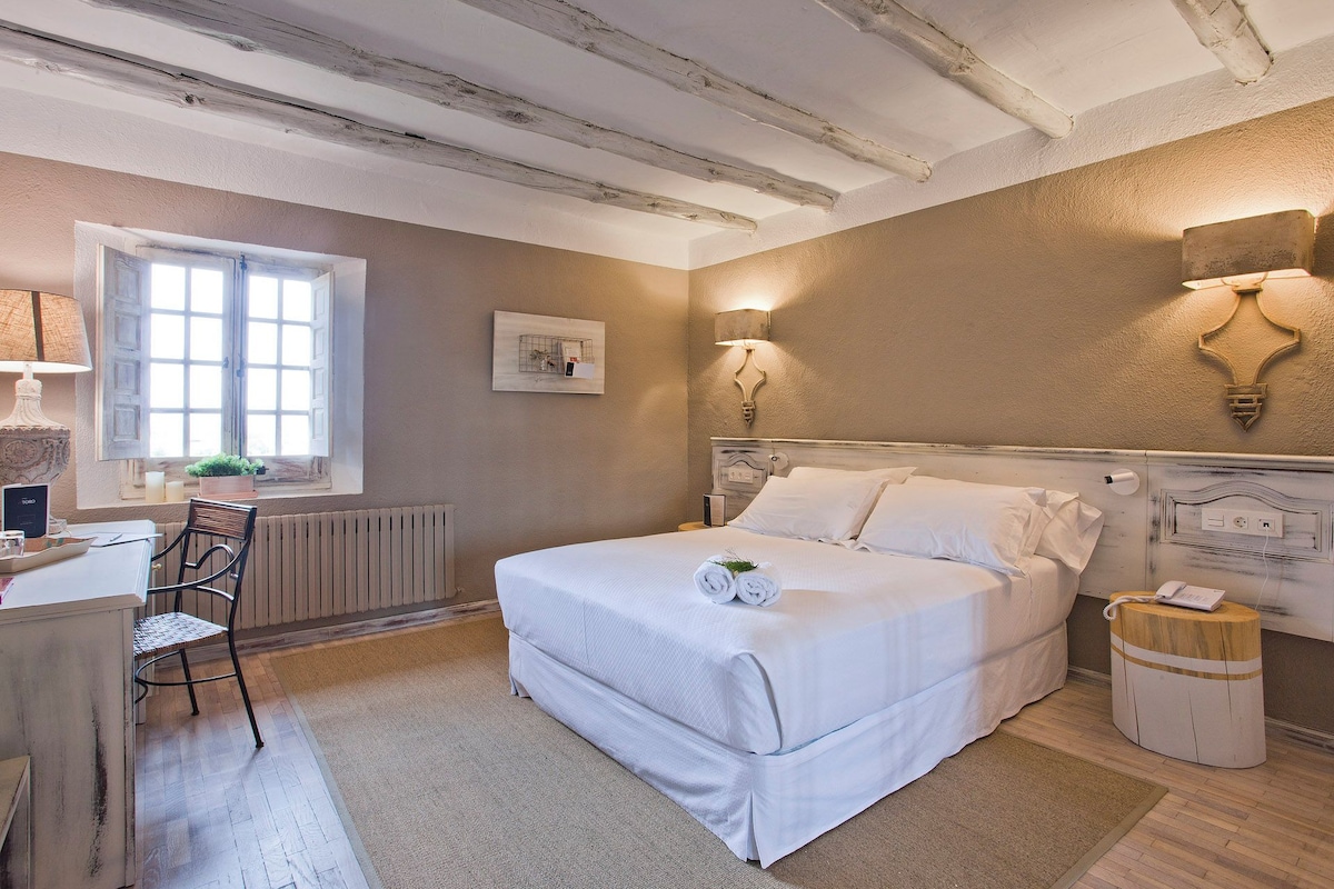 Un dormitorio con cama, mesita de noche, lámpara y ventana.