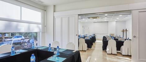 Une salle de conférence avec des tables disposées pour les réunions, des chaises et des bouteilles d’eau.