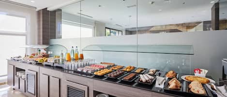 Un desayuno buffet moderno con diversas opciones de comida y bebidas, separadores de vidrio y un diseño limpio y contemporáneo.