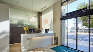 Un espace d’accueil moderne avec un comptoir de réception blanc, un vase rempli de fleurs jaunes et un tapis bleu sur lequel est inscrit le nom « Silk Hotel ».