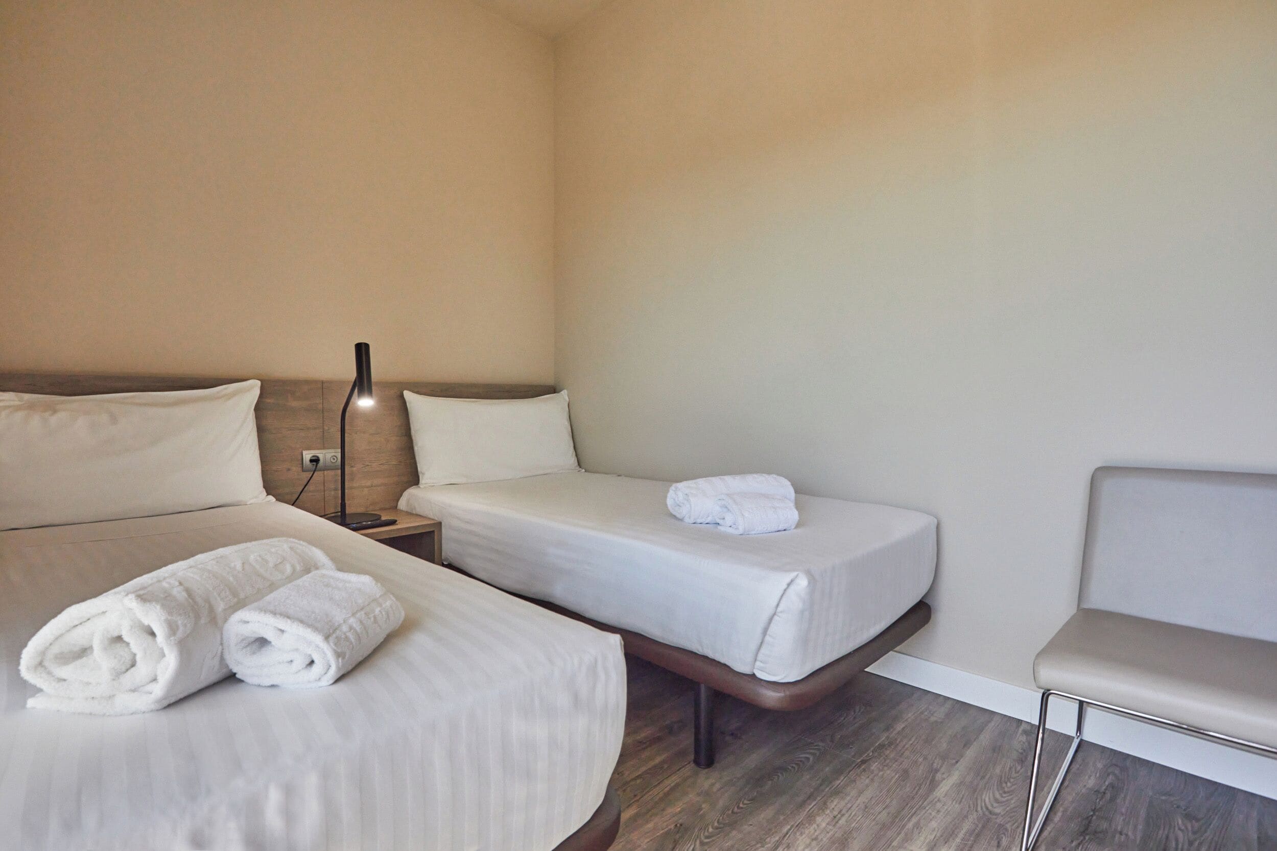 Una habitación de hotel con dos camas, una mesita de noche con lámpara y una silla.