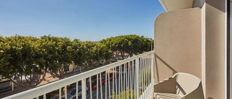 A balcony with a white railing overlooking a parking lot and trees.