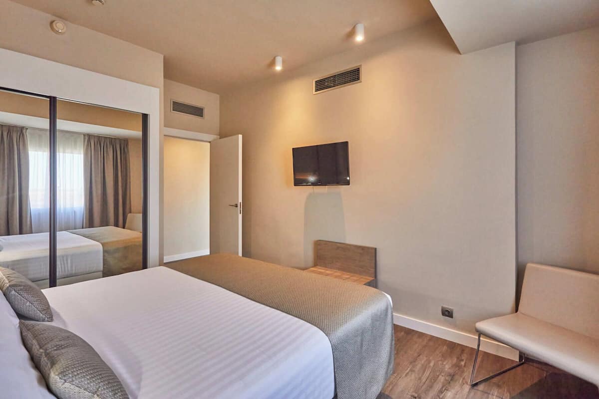 A hotel room with a large bed, a chair, a TV mounted on the wall, and a sliding door.