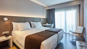 Une chambre d’hôtel avec deux lits, un bureau, une chaise et une grande fenêtre avec des rideaux.