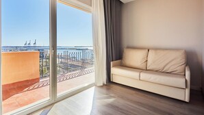 Un salon moderne avec un canapé beige, de grandes fenêtres et une vue sur un port avec des grues.