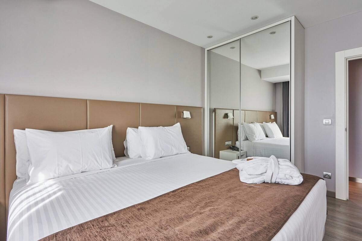 A modern hotel room with a large bed, a mirror, and a robe on the bed.