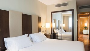 Habitación de hotel con una cama grande, una mesita de noche, un espejo y una puerta que da al baño.
