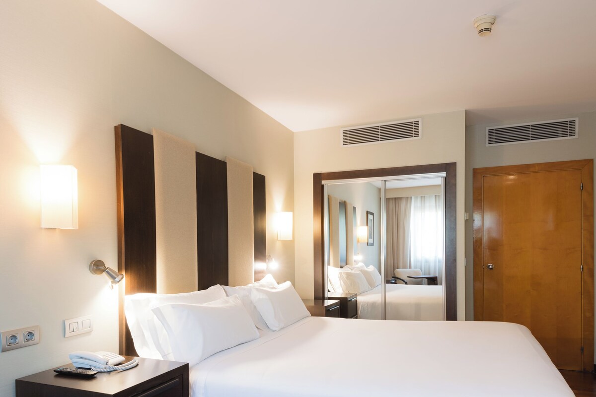 A hotel room with a large bed, a bedside table, a mirror, and a wardrobe.