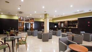 Un moderno espacio lounge con varias opciones de asientos, incluyendo mesas redondas y sofás, y una zona de bar con estantes llenos de botellas.