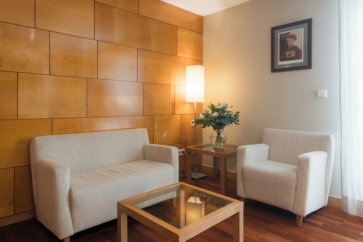 A modern living room with a wooden wall panel, a sofa, a chair, and a glass coffee table.