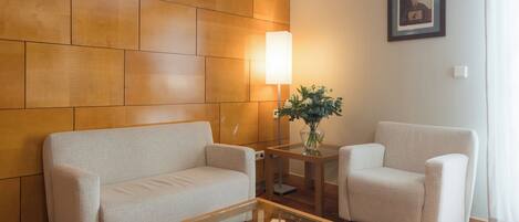 A modern living room with a wooden wall panel, a sofa, a chair, and a glass coffee table.