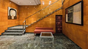 Un vestíbulo con una escalera de mármol, un sofá rojo, una mesa de centro de cristal y una barandilla de escalera.