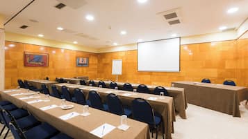 Un salón de conferencias con mesas largas, sillas y una pantalla para proyector.