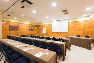 Une salle de conférence équipée de longues tables, de chaises et d’un écran de projection.