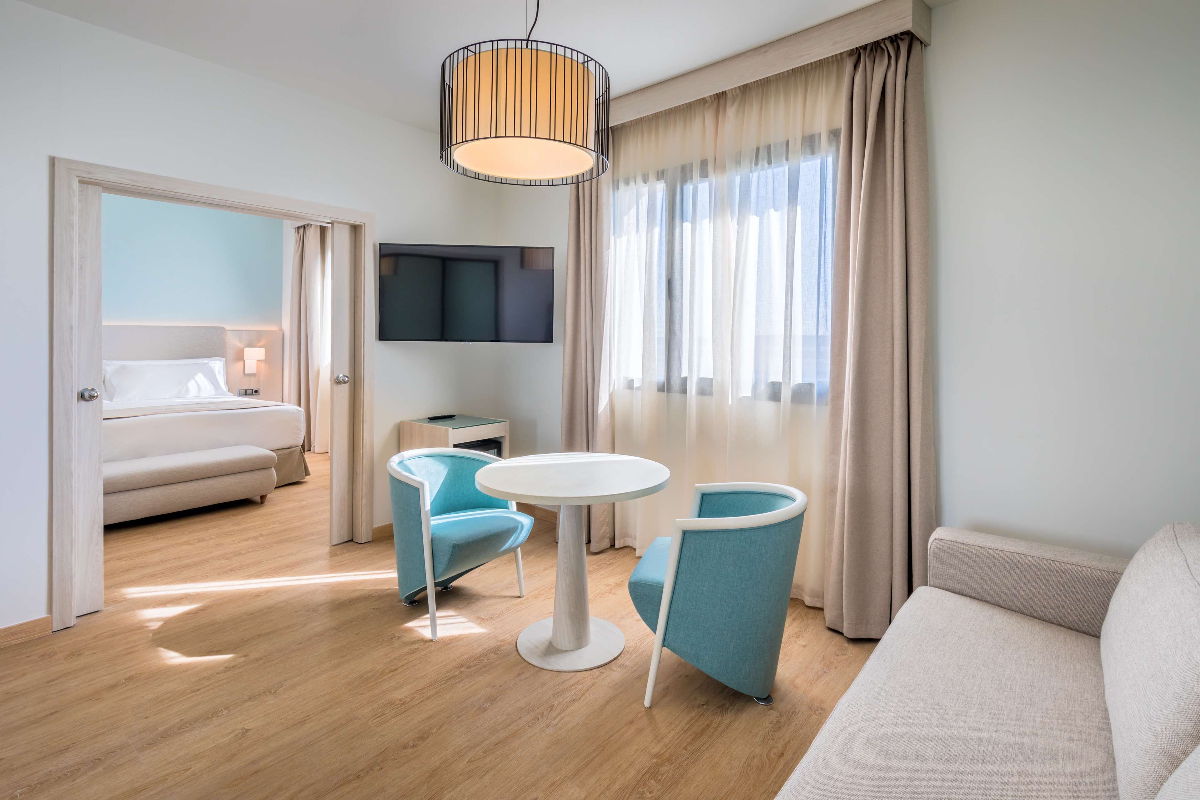 Una habitación de hotel moderna con sofá, dos sillones, una mesa redonda, televisor y cama.