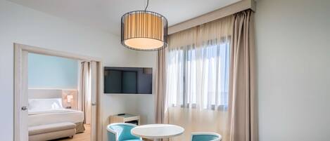A modern hotel room with a sofa, two chairs, a round table, a TV, and a bed.