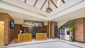 Een moderne lobby met een receptiebalie, een digitaal scherm en een koffieapparaat.
