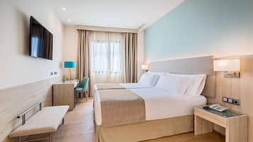 Habitación de hotel con dos camas, un escritorio, un banco y un televisor montado en la pared.