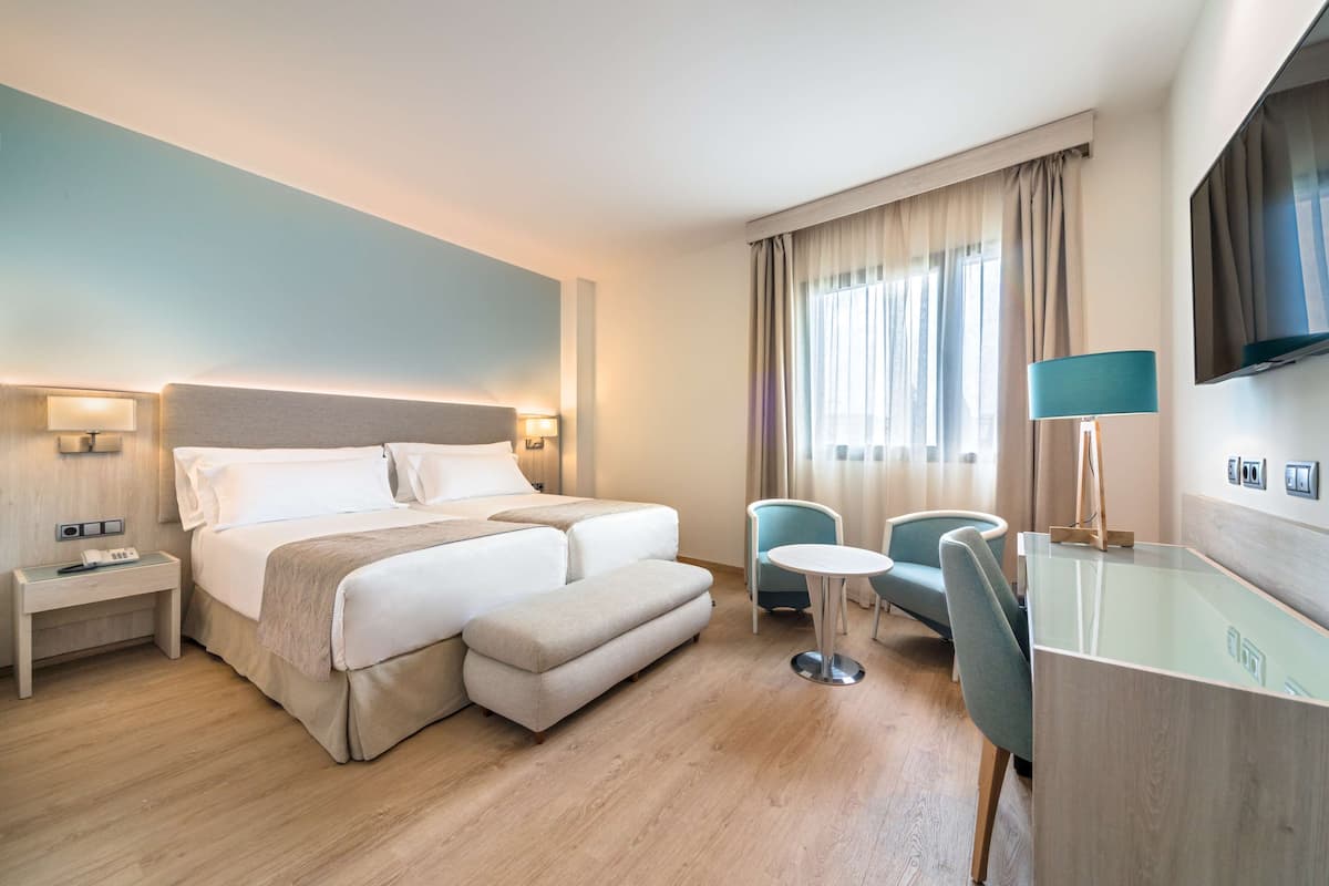 Habitación de hotel con una cama grande, mesitas de noche, un escritorio con silla y televisor montado en la pared.