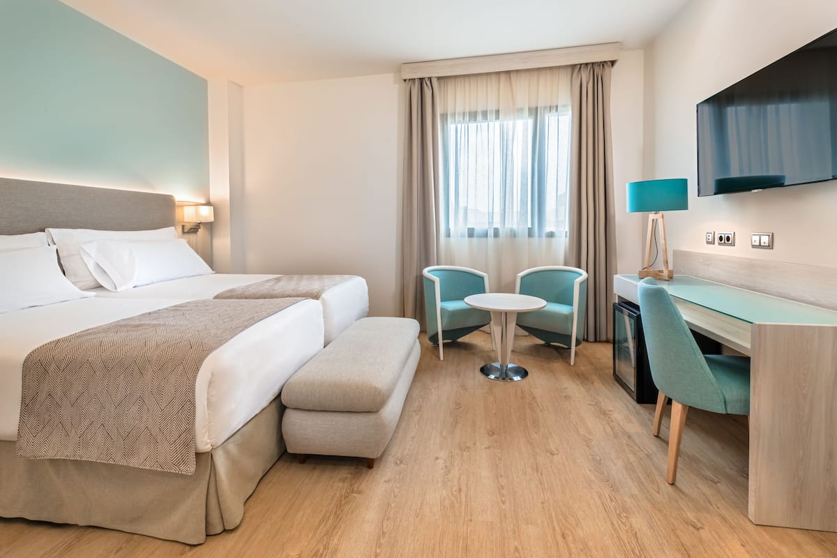 Una habitación de hotel con una cama, un escritorio con silla, una mesita y un televisor montado en la pared.