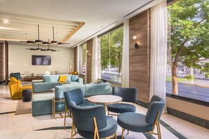 A modern hotel lobby with a seating area, large windows, and a flat-screen TV.