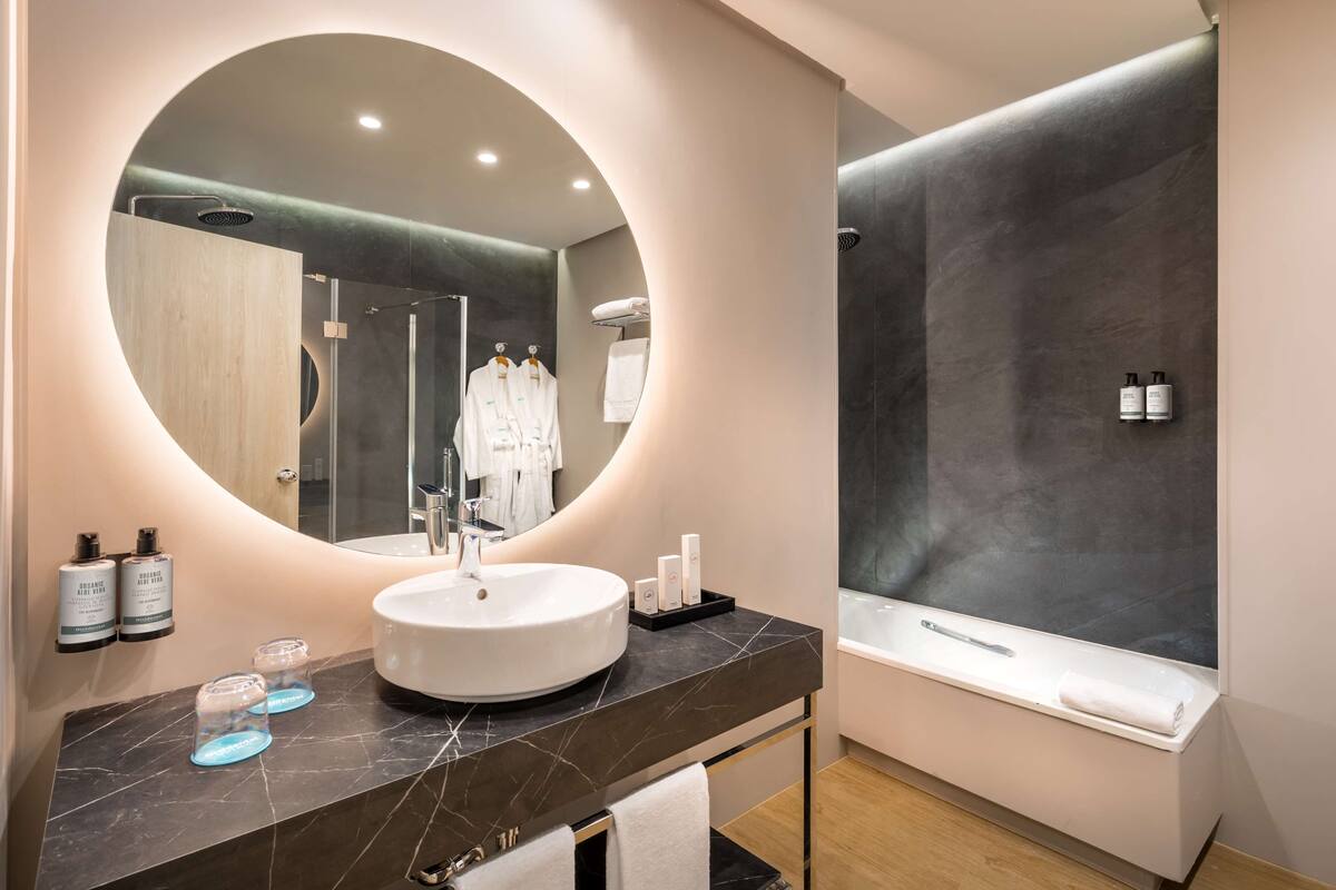 Ein modernes Badezimmer mit einem runden Spiegel, einem Waschbecken, einer Badewanne und einer Dusche.