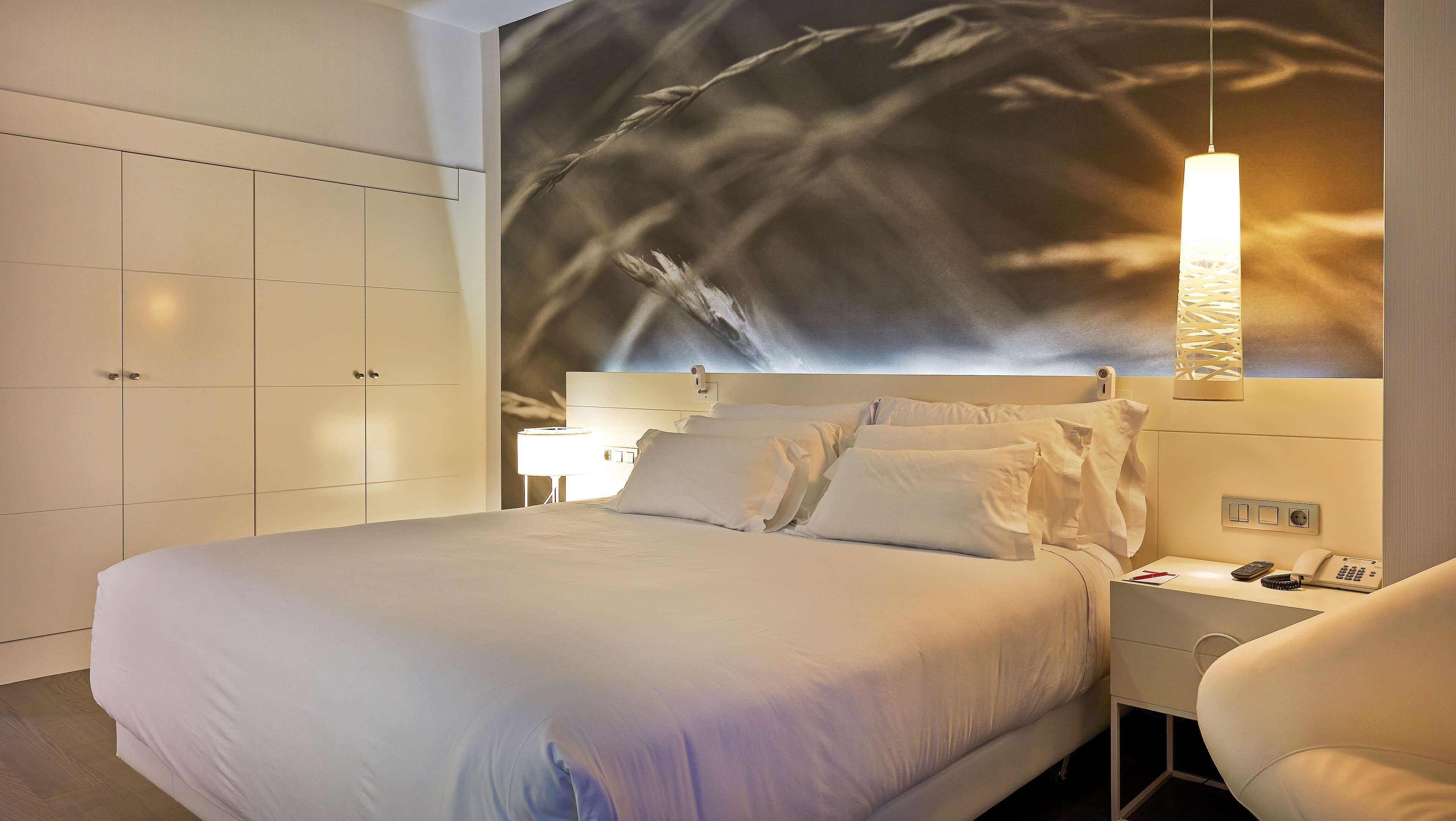 Habitación de hotel moderna con una cama grande, una mesita de noche, una silla y una lámpara fijada a la pared.