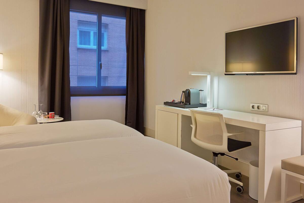 Une chambre d’hôtel avec un grand lit, un bureau avec un ordinateur, une chaise, une lampe et un téléviseur fixé au mur.