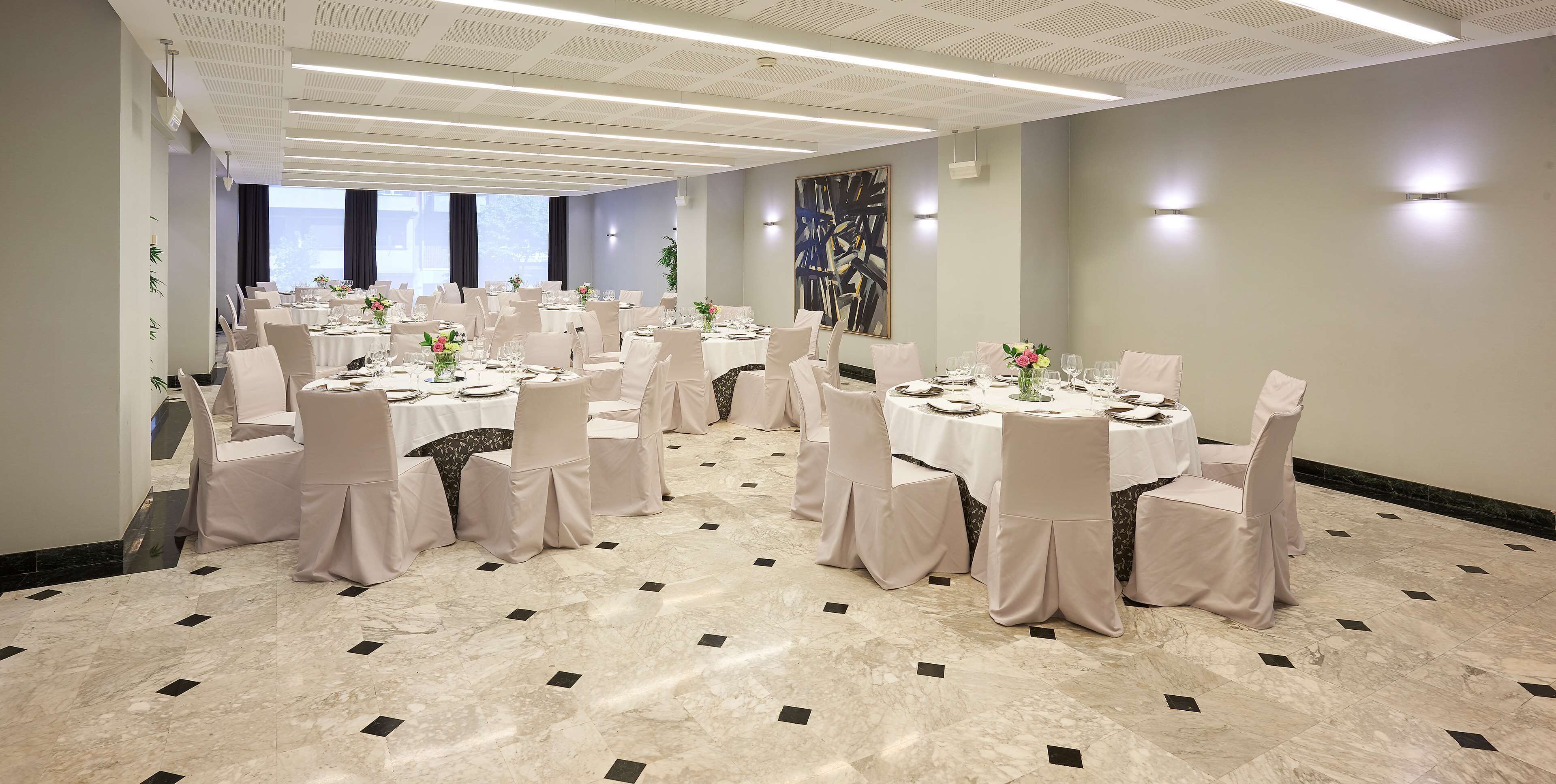 A banquet hall with round tables, white chairs, and a marble floor.