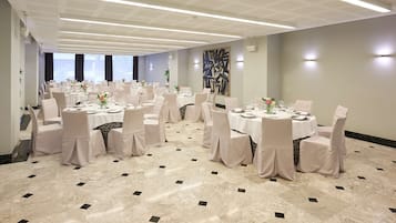 A banquet hall with round tables, white chairs, and a marble floor.