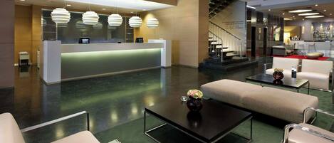 A modern hotel lobby with a reception desk, seating area, and staircase.